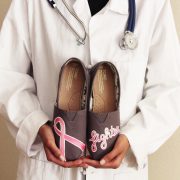 Custom, hand painted Breast Cancer Fighter grey TOMS shoes featuring the word "fighter" and the pink breast cancer awareness ribbon. Held by doctor.